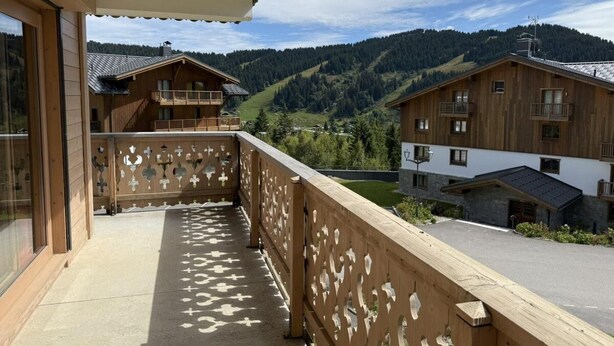A wooden balcony with patterned railings overlooking a mountainous landscape.