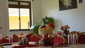 A dining table set with a red tablecloth, clear glassware, and a centerpiece of white and red flowers. - BAVAH AIRPORT HOTEL (Entebbe)