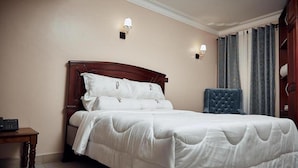 A neatly made bed with white bedding, a wooden headboard, and two wall-mounted reading lamps. - BAVAH AIRPORT HOTEL (Entebbe)