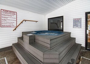 Un jacuzzi con escalones que conducen hacia él, rodeado de paredes blancas y una terraza de madera.