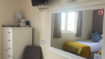 Een slaapkamer met een bed, een dressoir, een stoel, een televisie en een spiegel.