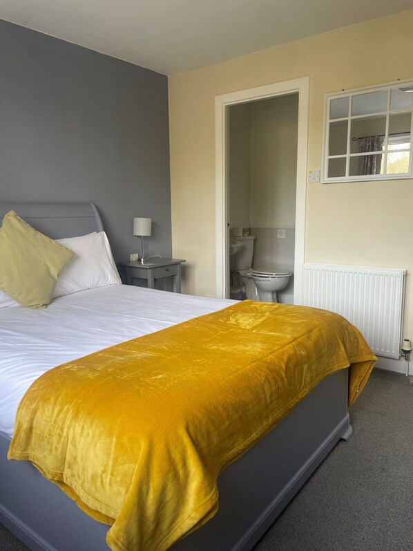 A bedroom with a bed, a bedside table, a lamp, and a window.