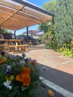 Un patio al aire libre con mesas de picnic de madera y una zona cubierta para sentarse.