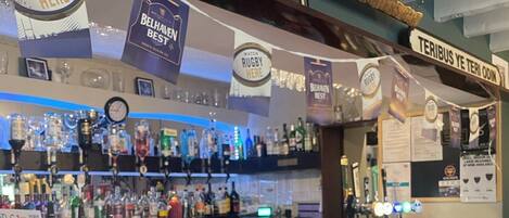 A bar area with a counter, various bottles, and a sign that reads "RUGBY HERE".