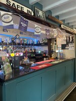 Una zona de bar con mostrador, varias botellas y un letrero que dice "RUGBY HERE".