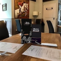 Una mesa de comedor con un atril para menú, un cuadro enmarco de caballos y un perchero.