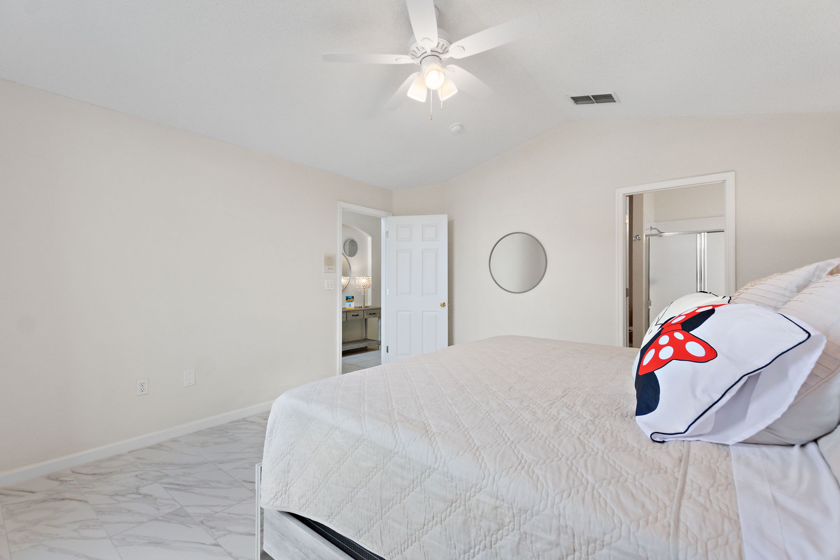 A bedroom with a bed, a ceiling fan, a door, and a bathroom visible through an open door.