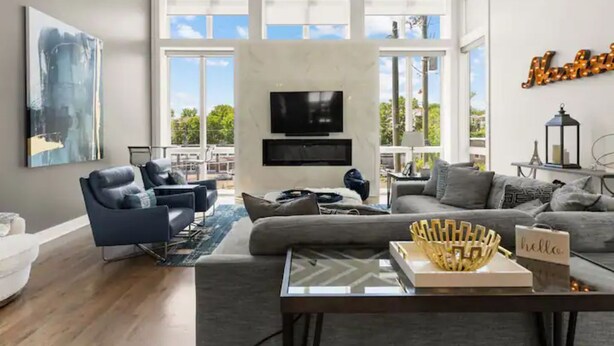 A modern living room with a large window, a flat-screen TV, and a sofa. - Always A Guest Favorite! Luxe 3 Level Home+ HUGE Rooftop Deck w/TV, fireplace! (Berry Hill)