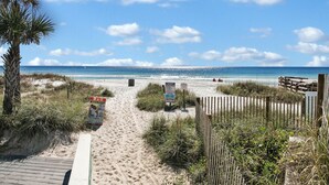 A sandy beach path leading to the ocean with a wooden fence and a palm tree on the left.