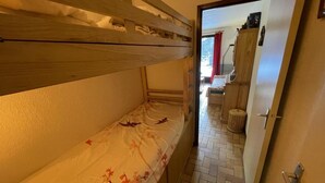 Kerrossängyllä varustettu huone, jossa on laattalattia, puuovi ja käytävä, joka johtaa kylpyhuoneeseen.