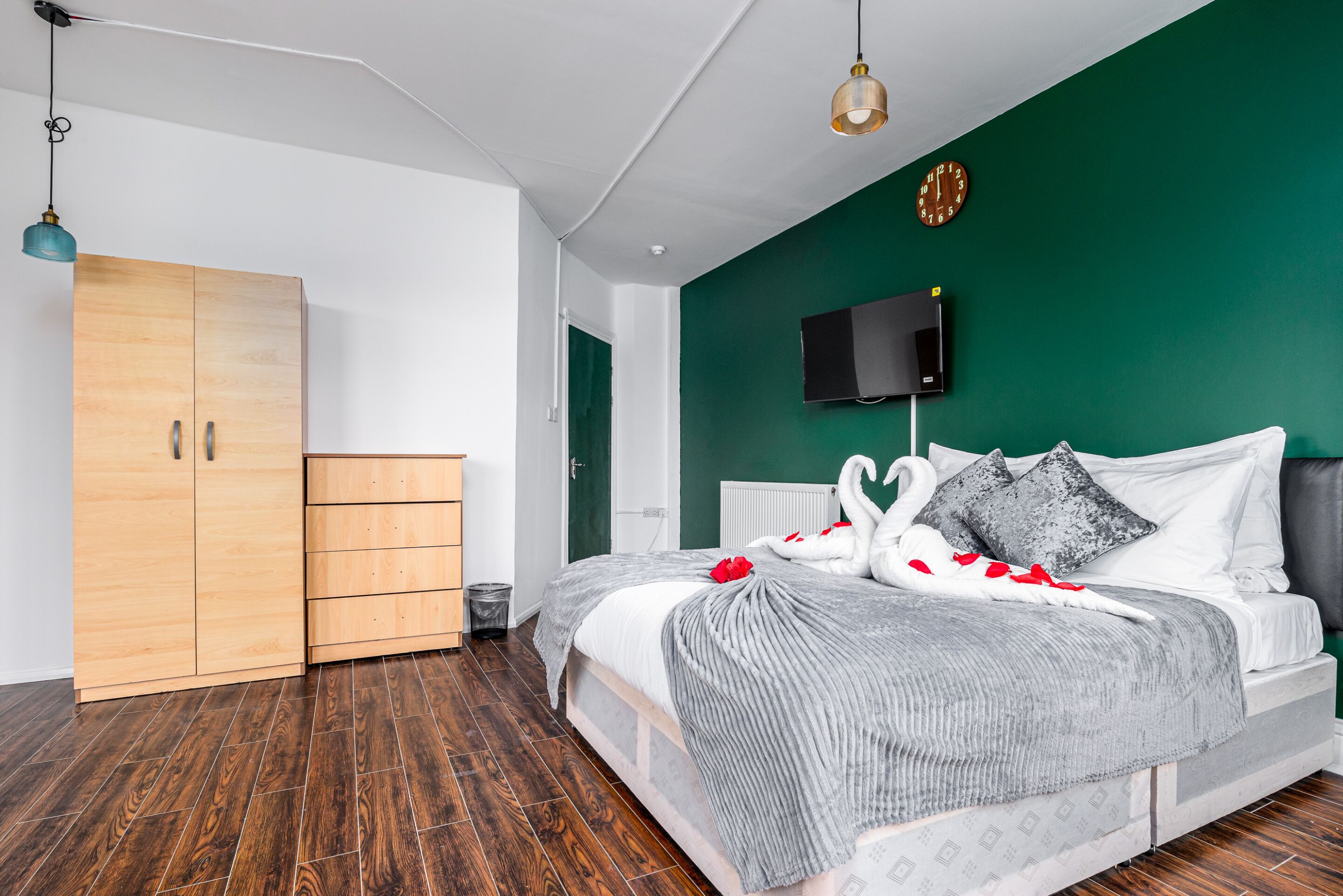 A modern bedroom with a large bed, a wardrobe, a television, and a green accent wall.