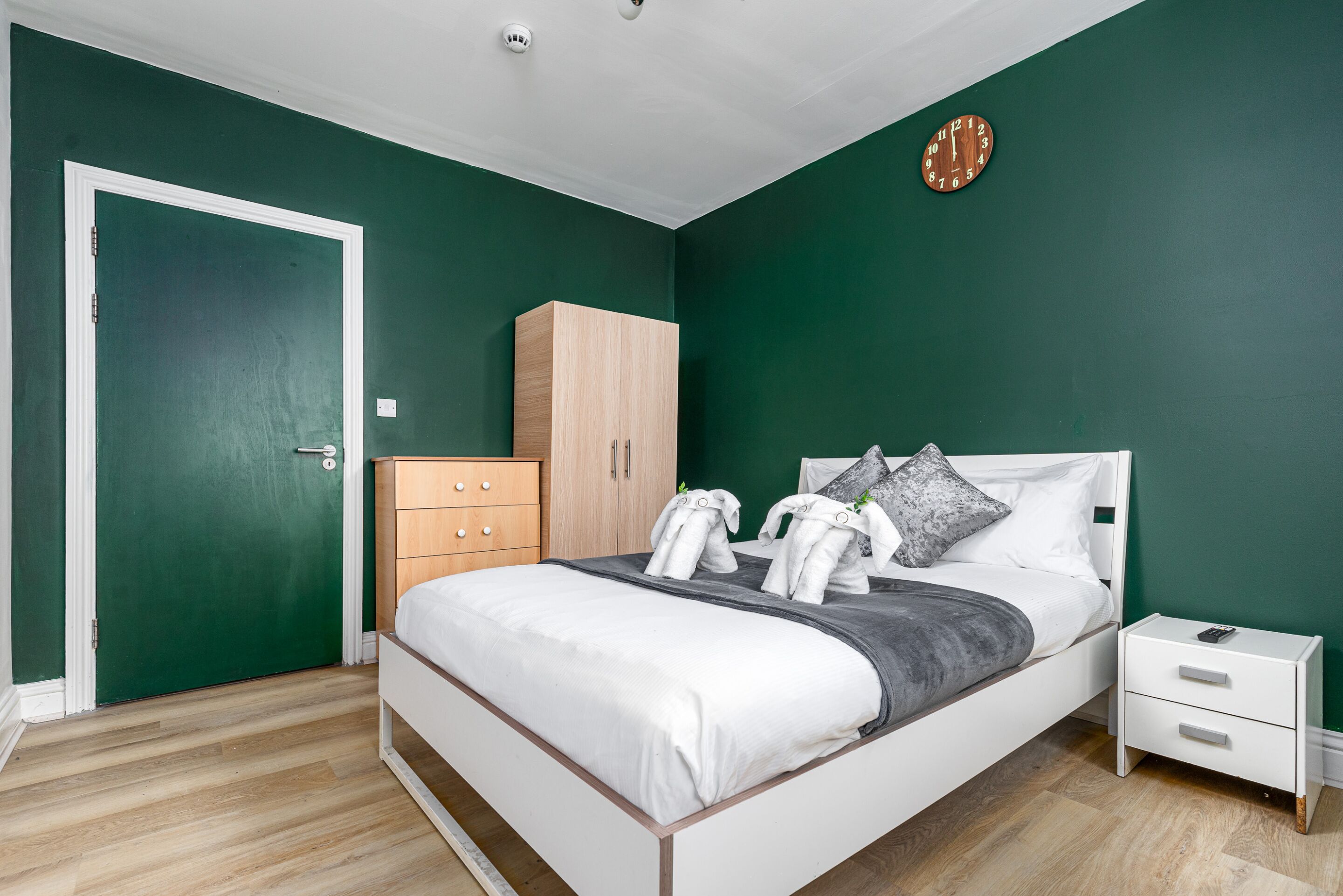 Een slaapkamer met een bed, nachtkastje, kapstok en een deur.