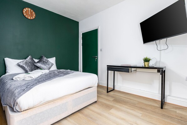 A bedroom with a bed, a desk, a TV, and a green door. - City Gate Guest House (London)