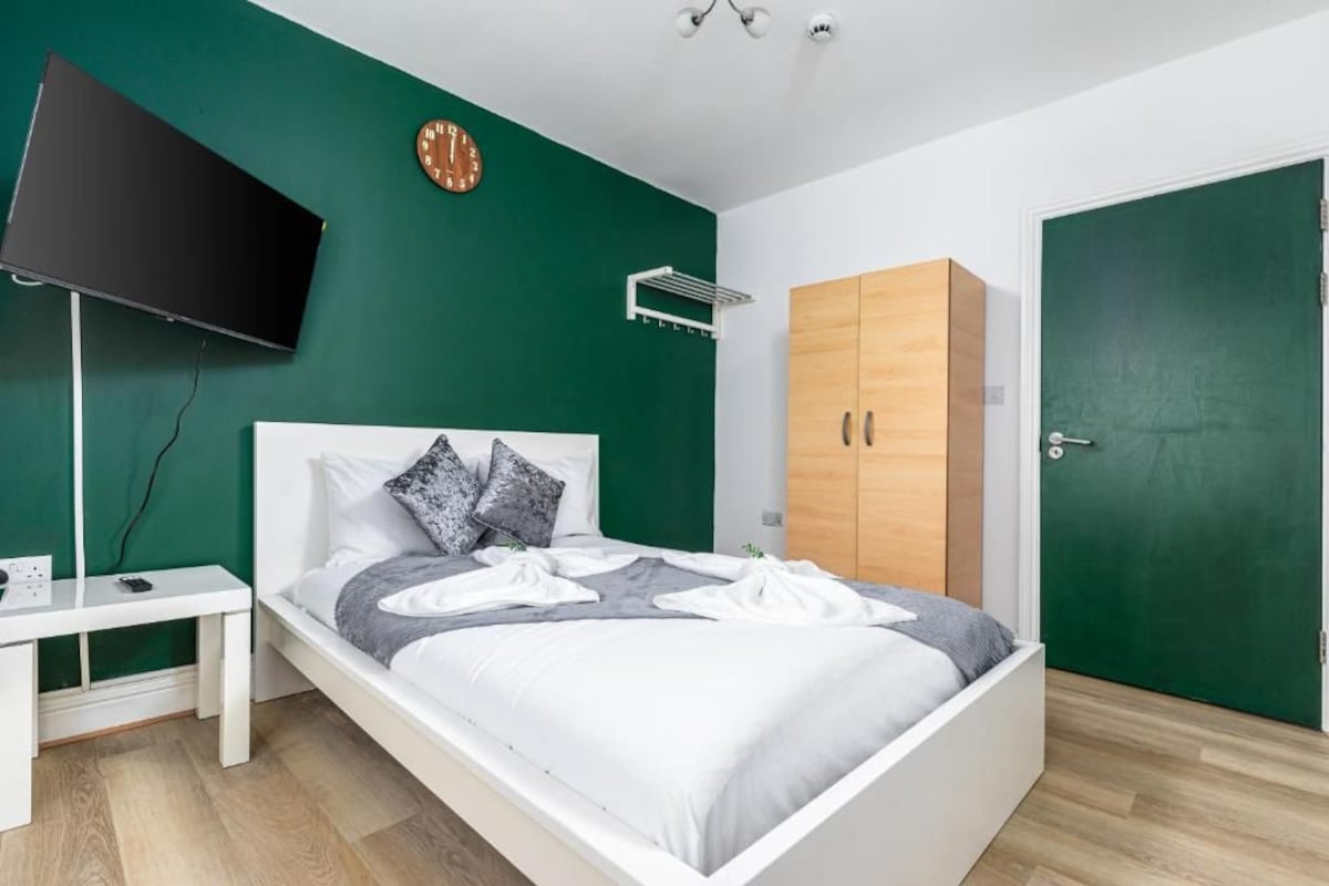 A modern bedroom with a bed, a TV, a clock, and a wardrobe.