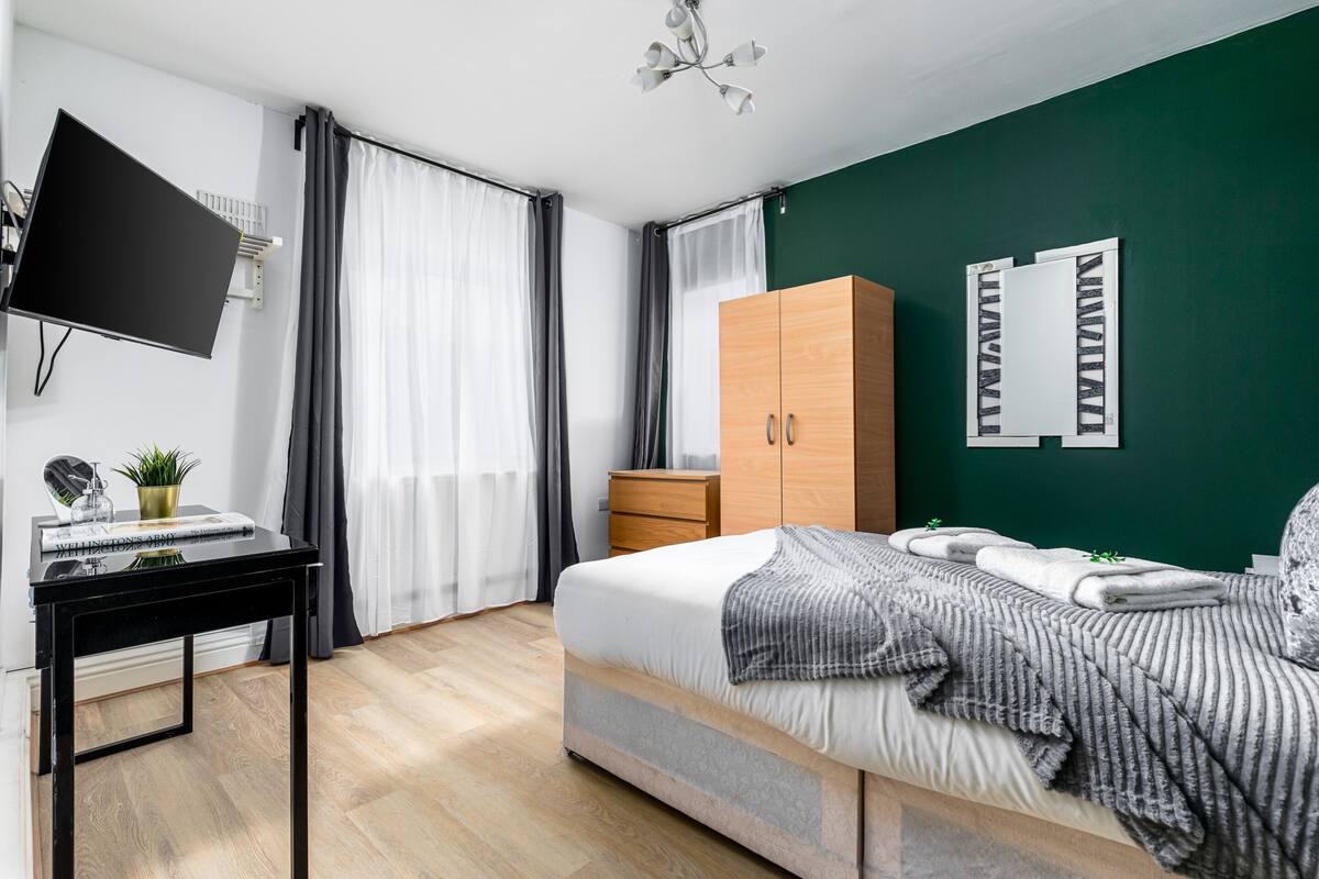 A modern bedroom with a bed, a desk, a wardrobe, a TV, and a mirror.
