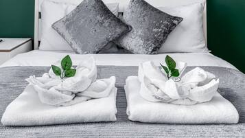 A neatly made bed with white linens and two towels with green leaves, a gray blanket, and two gray pillows on a green wall background.