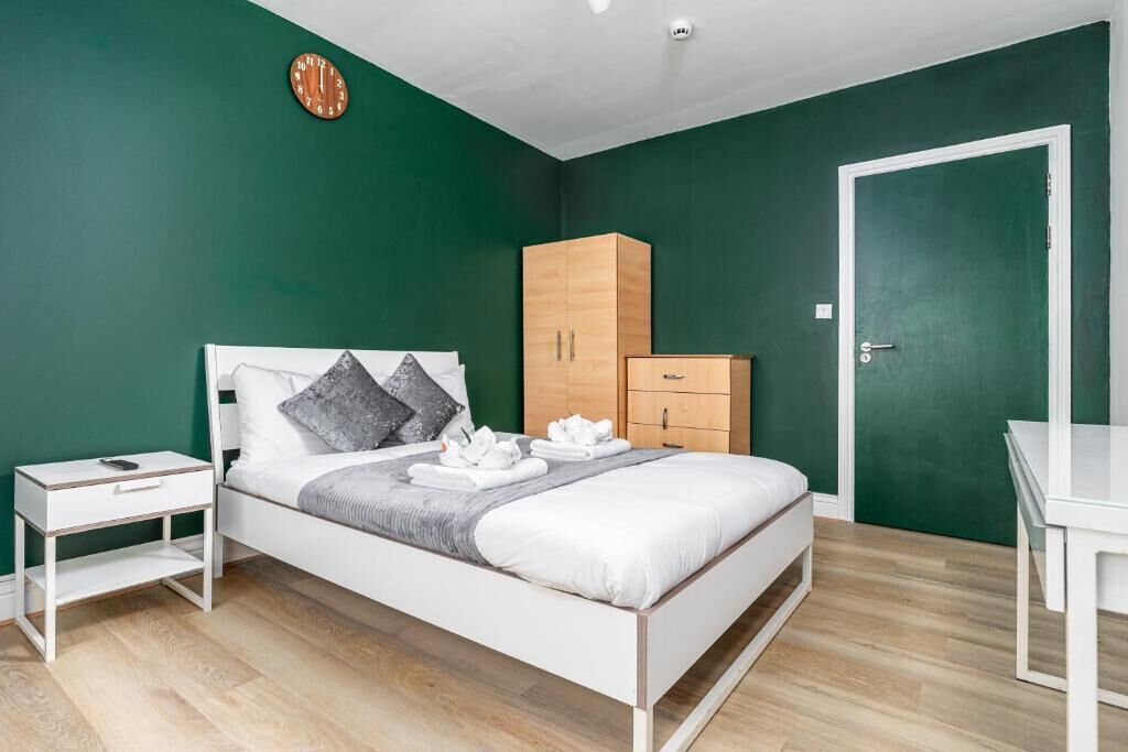 Une chambre à coucher avec un lit, une armoire en bois, une table de chevet blanche et un mur vert.