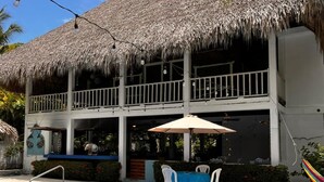 Ein Poolbereich mit einem strohgedeckten Gebäude, Sitzmöglichkeiten im Freien und einer Bar.