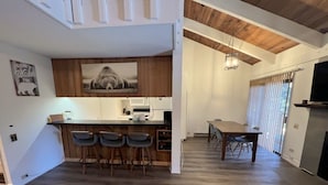 A modern kitchen with a bar area, wooden flooring, and a dining table with chairs. - 118 Standard 2 Bedroom Condo by RedAwning (Mammoth Lakes)
