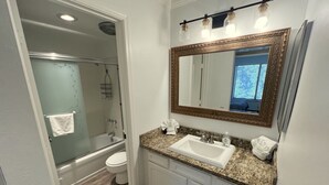 A bathroom with a granite countertop sink, a large mirror with a gold frame, and a shower area. - 118 Standard 2 Bedroom Condo by RedAwning (Mammoth Lakes)