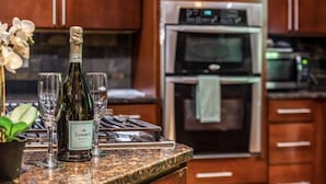 Une cuisine équipée d’un four et d’un micro-ondes en acier inoxydable, une bouteille de vin et des verres à vin posés sur le comptoir.