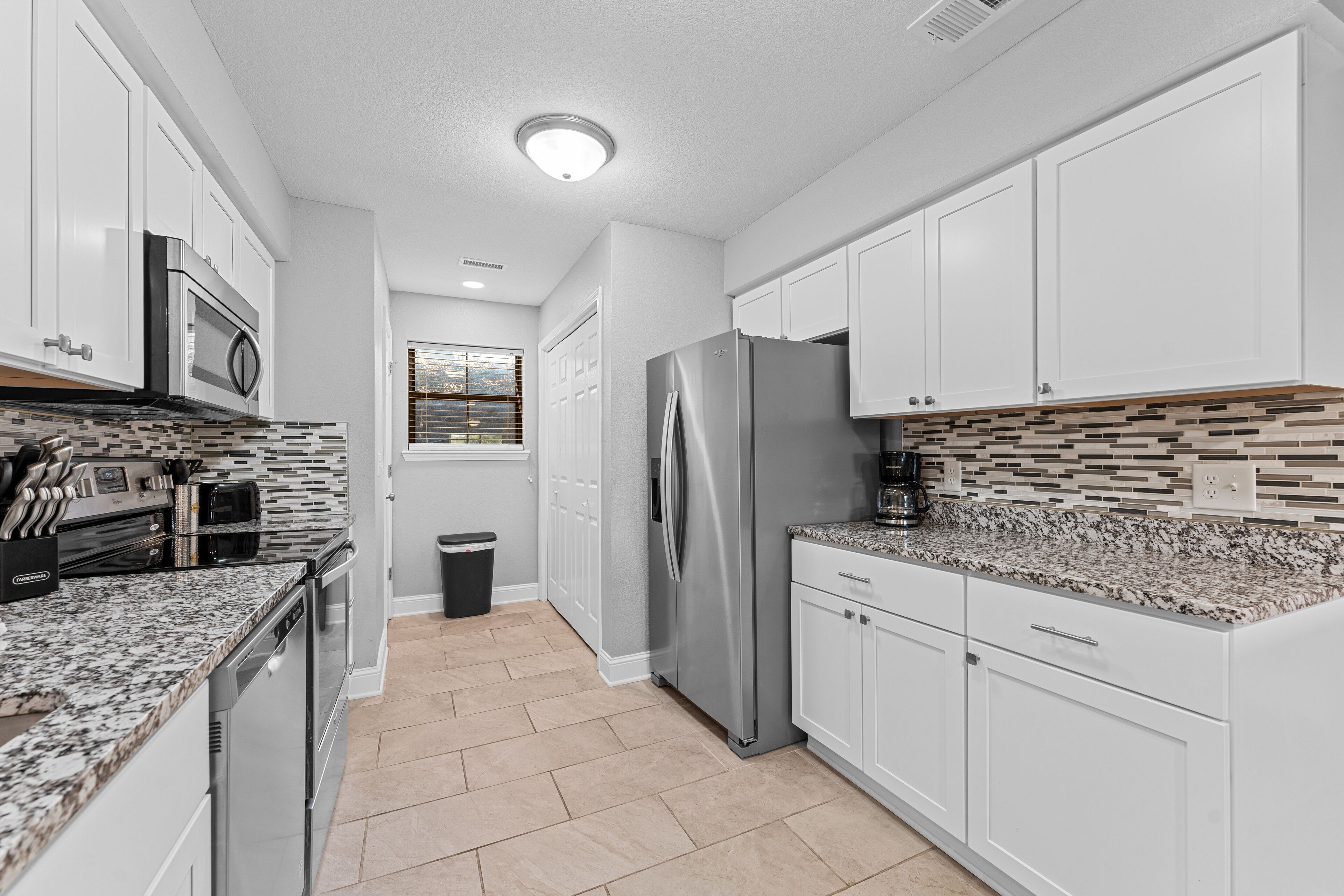 A modern kitchen with white cabinets, stainless steel appliances, and a patterned backsplash.