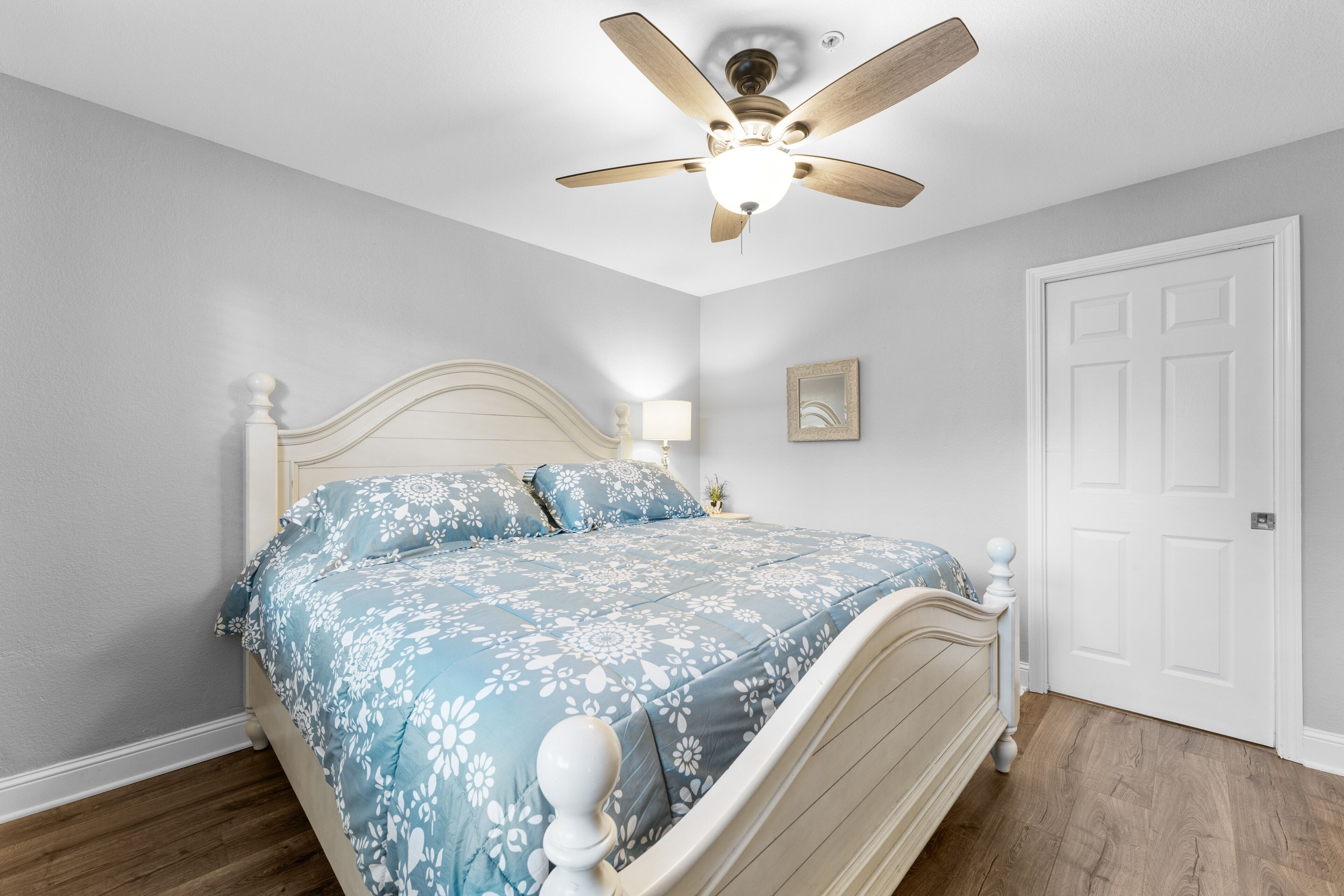 Ein Schlafzimmer mit Bett, Deckenventilator, Tür und Nachttisch mit Lampe.