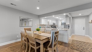 Una cocina moderna con armarios blancos, una isla central y una zona de comedor con sillas y mesa de madera.