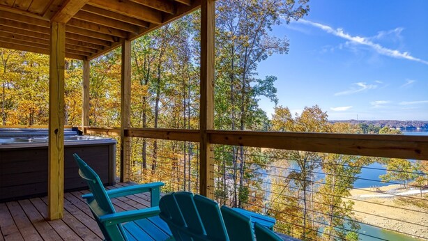 A covered deck with wooden railings, a hot tub, and green Adirondack chairs overlooking a lake and autumn foliage. - Smoky Lake Retreat 3 Bedroom Cabin by RedAwning (Dandridge)