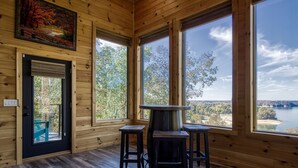 A cabin interior with large windows, a wooden floor, and a central table with chairs. - Smoky Lake Retreat 3 Bedroom Cabin by RedAwning (Dandridge)