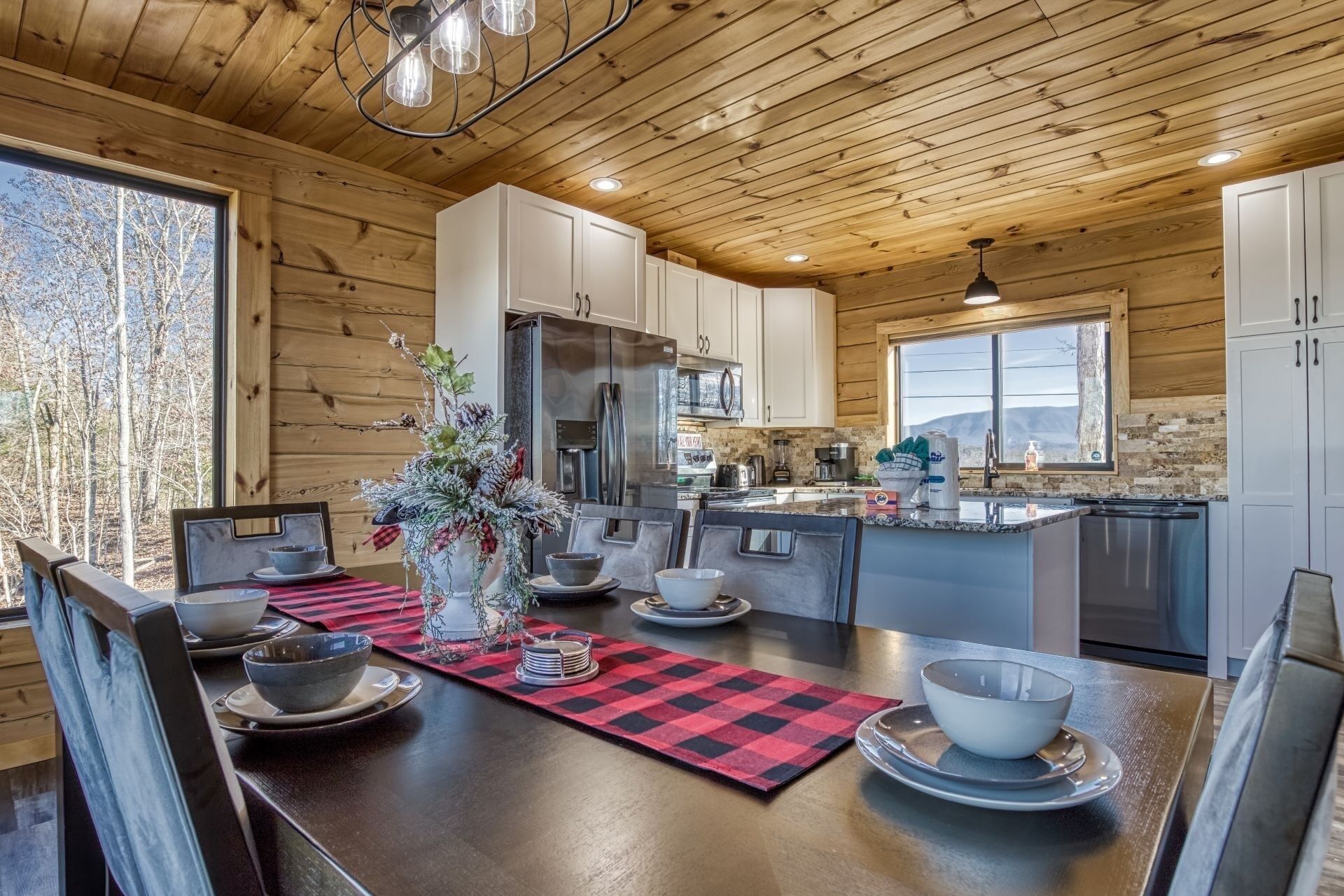 Une cuisine moderne avec des meubles en bois, un îlot central et un coin repas agrémenté d’un set de table à carreaux rouges et noirs.