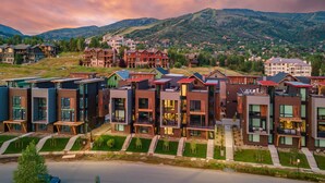 Un quartier résidentiel moderne avec des immeubles à plusieurs étages, un petit plan d’eau et un paysage vallonné en arrière-plan.
