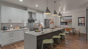 Une cuisine moderne dotée d’un îlot central, d’appareils électroménagers en acier inoxydable et de luminaires suspendus.