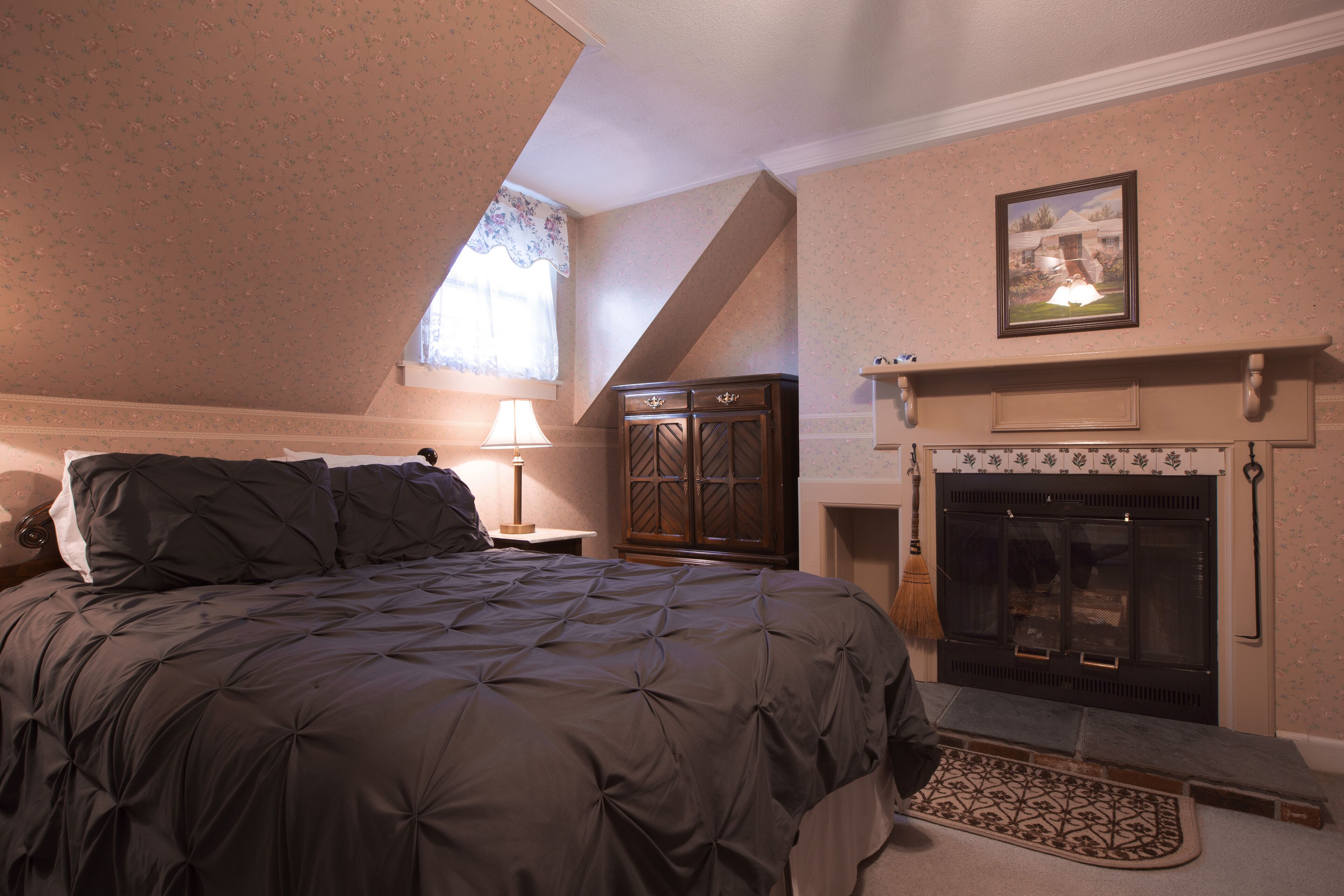 Een slaapkamer met een groot bed, een houten kast, een open haard en een raam met een bloemen gordijn.