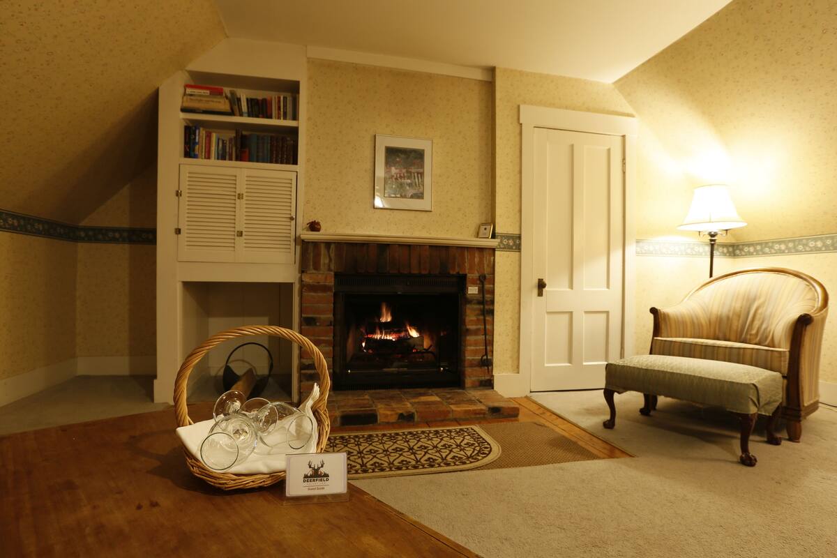 A cozy living room with a fireplace, a bookshelf, a wicker basket with glasses, and a lamp.