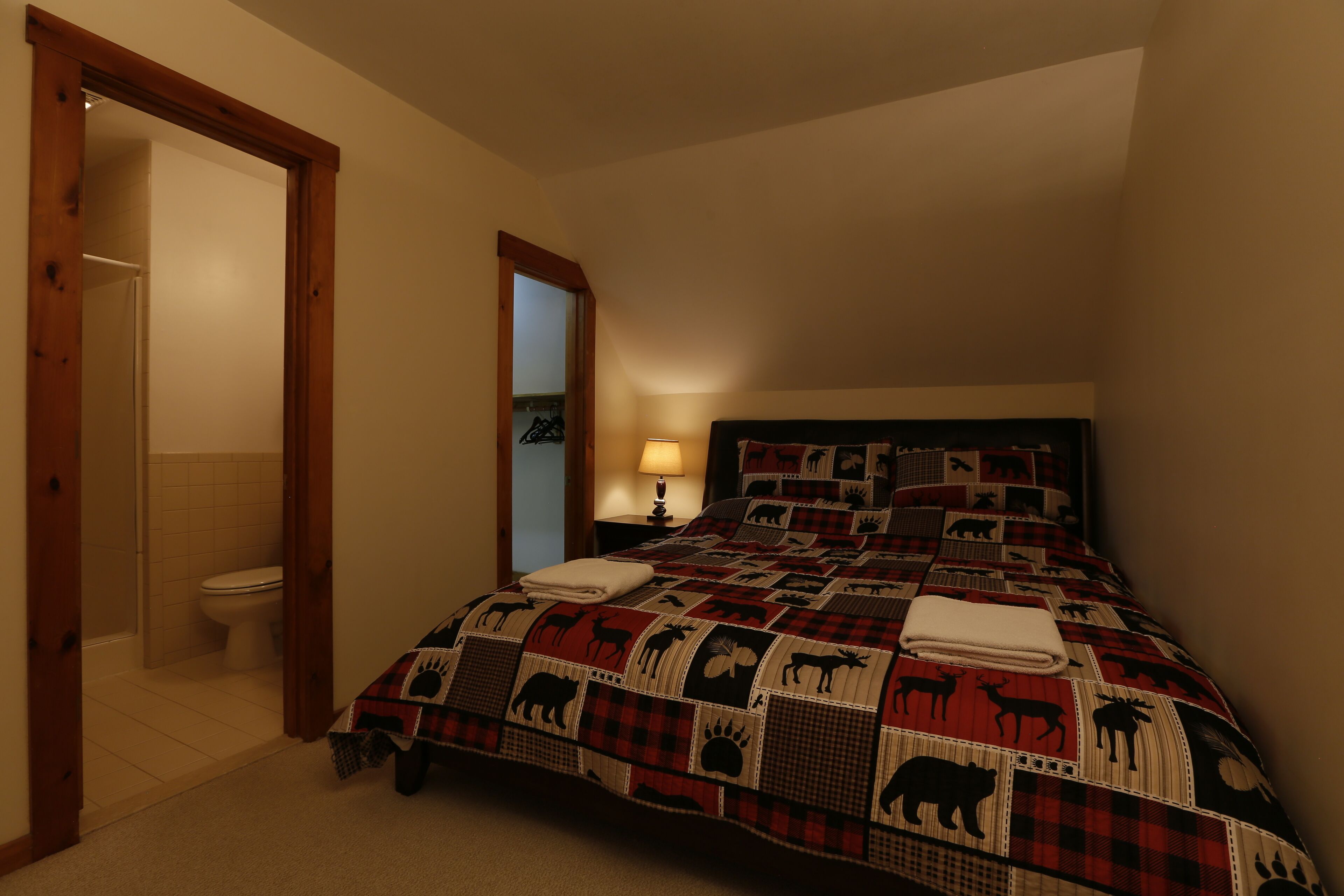 A bedroom with a bed featuring a red and black plaid pattern, a wooden headboard, and a nightstand with a lamp.