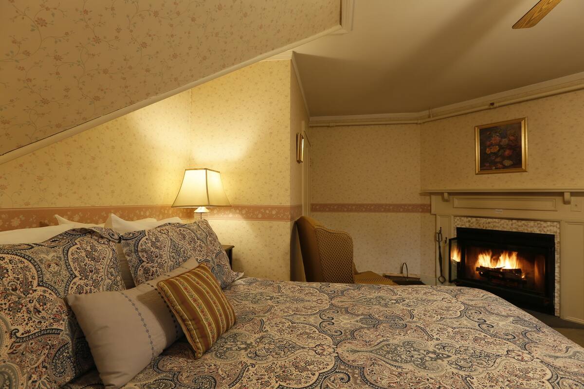 A bedroom with a large bed, a fireplace, and a nightstand.