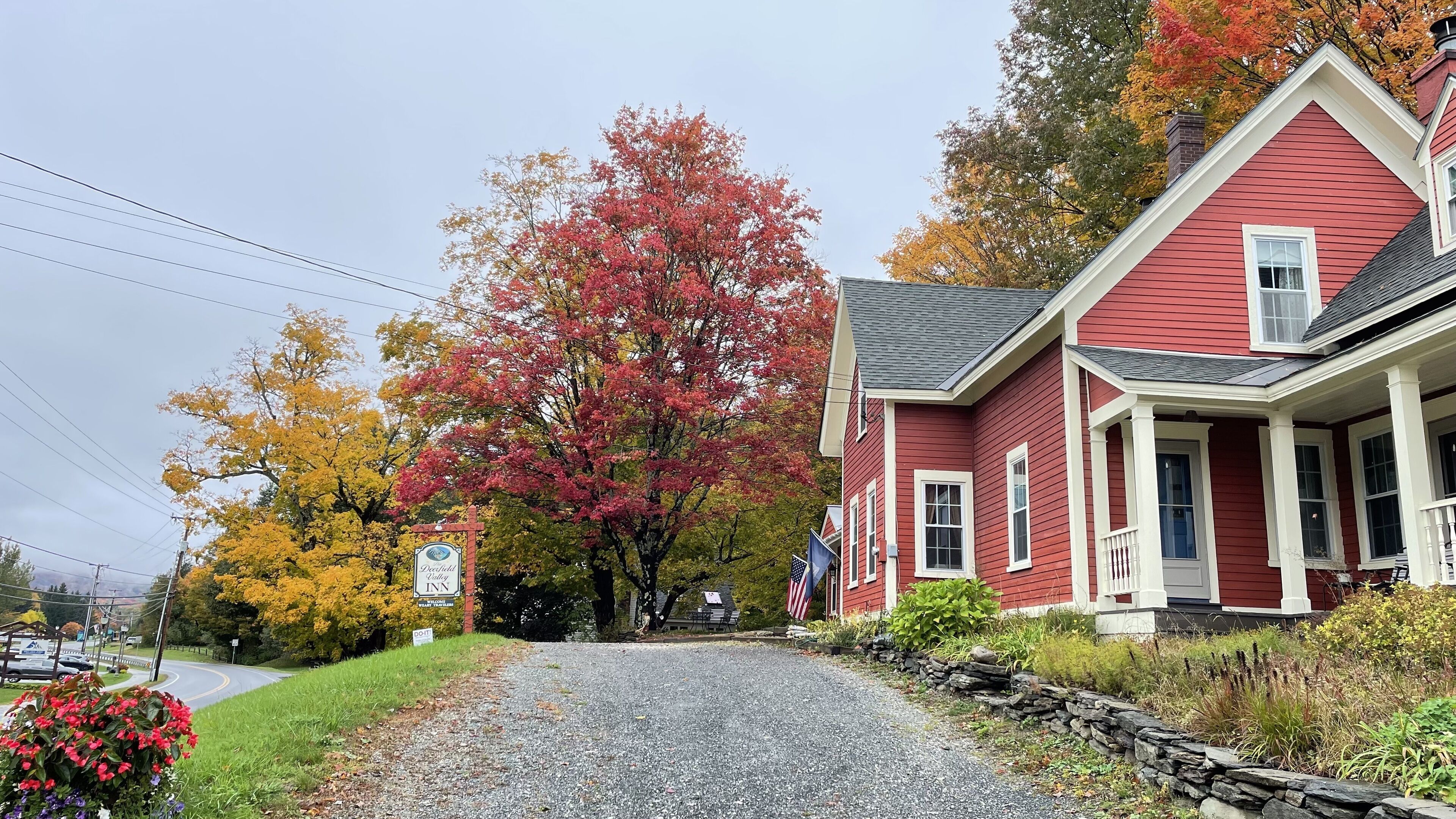 A red building with a porch, a gravel driveway, and autumn foliage.