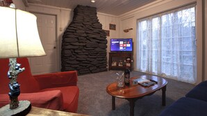 Una sala de estar con pared de piedra, televisor y chimenea.