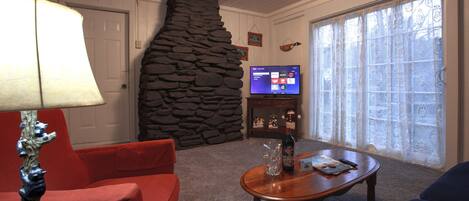 Una sala de estar con pared de piedra, televisor y chimenea.