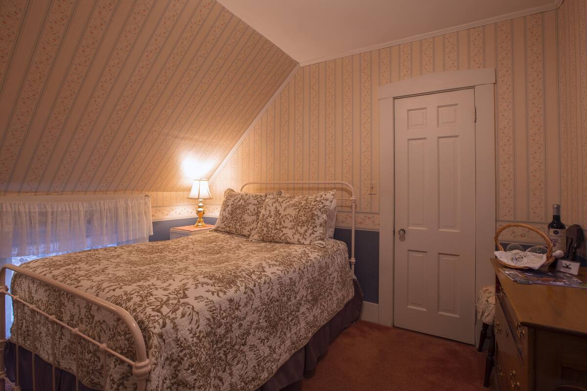 A bedroom with a bed, a nightstand, a lamp, a dresser, and a door.