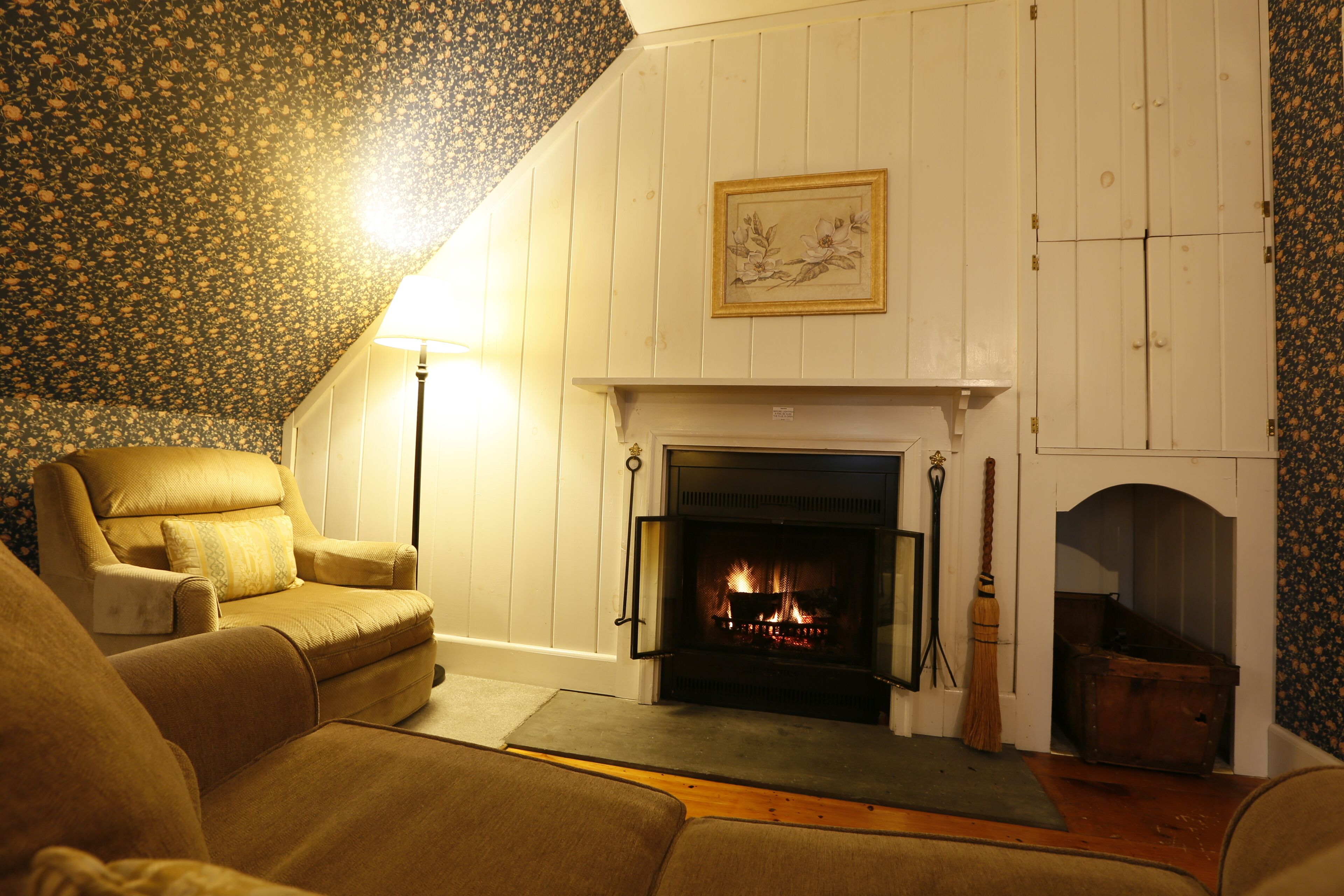 A cozy living room with a fireplace, a comfortable armchair, and a patterned wallpaper.