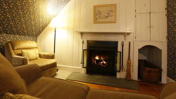A cozy living room with a fireplace, a comfortable armchair, and a patterned wallpaper.