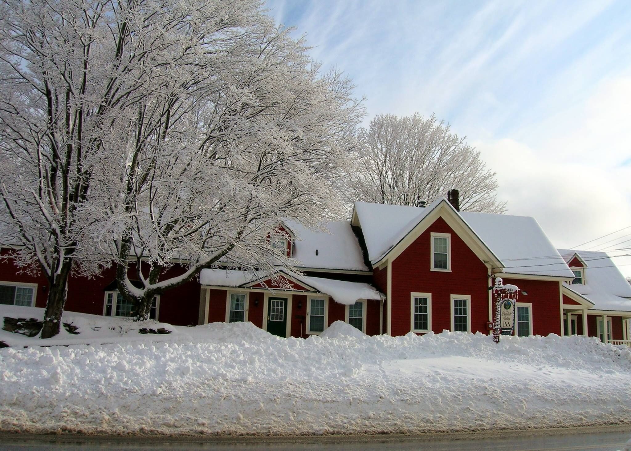 A red house with a snow-covered roof and a large tree in front.