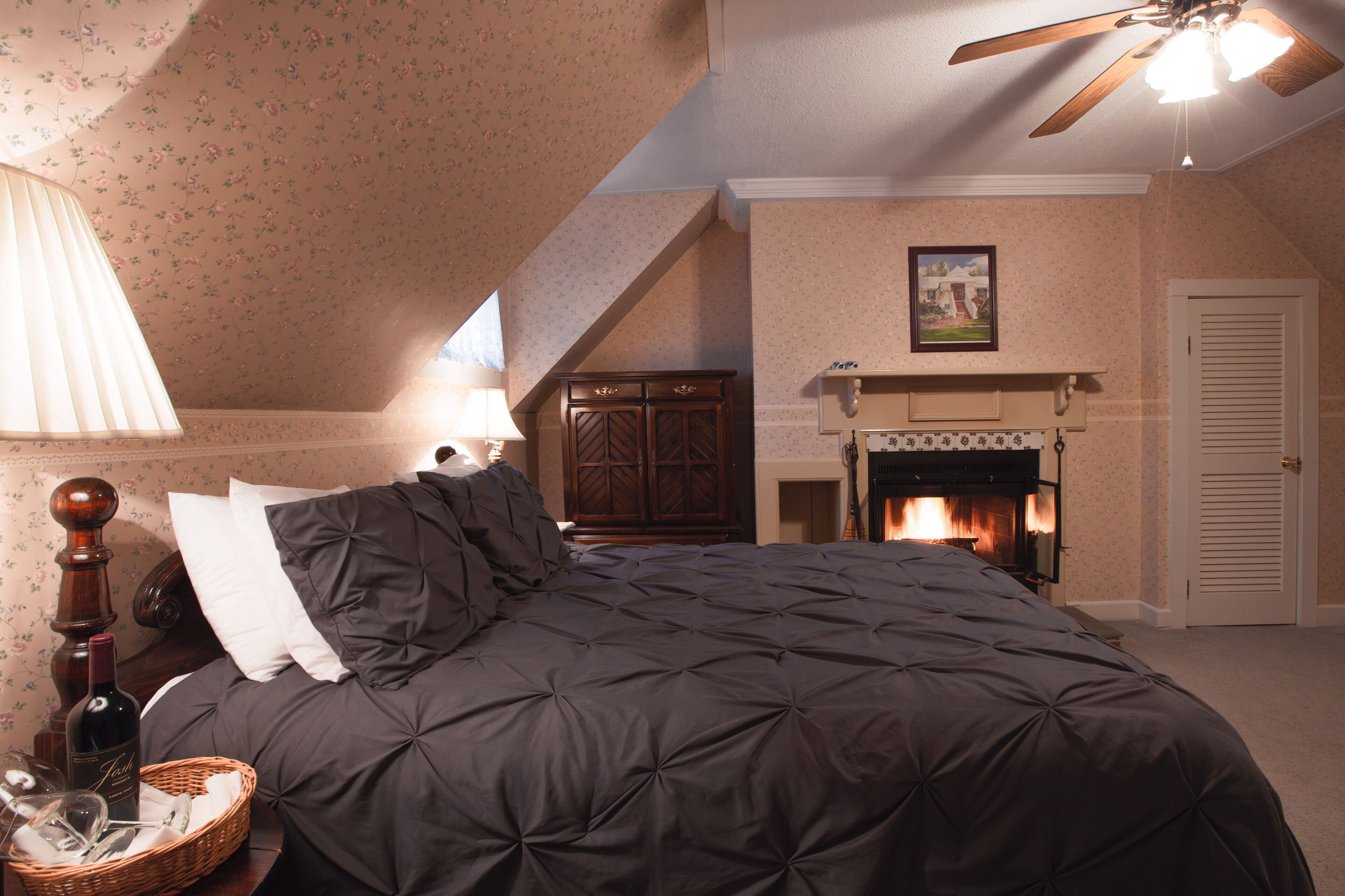Une chambre à coucher avec une couvre-lit matelassé de couleur sombre, une tête de lit en bois, une cheminée et un ventilateur de plafond.