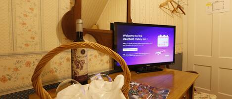 A room with a television displaying a welcome message, a wicker basket with a bottle, and a magazine on a wooden table.