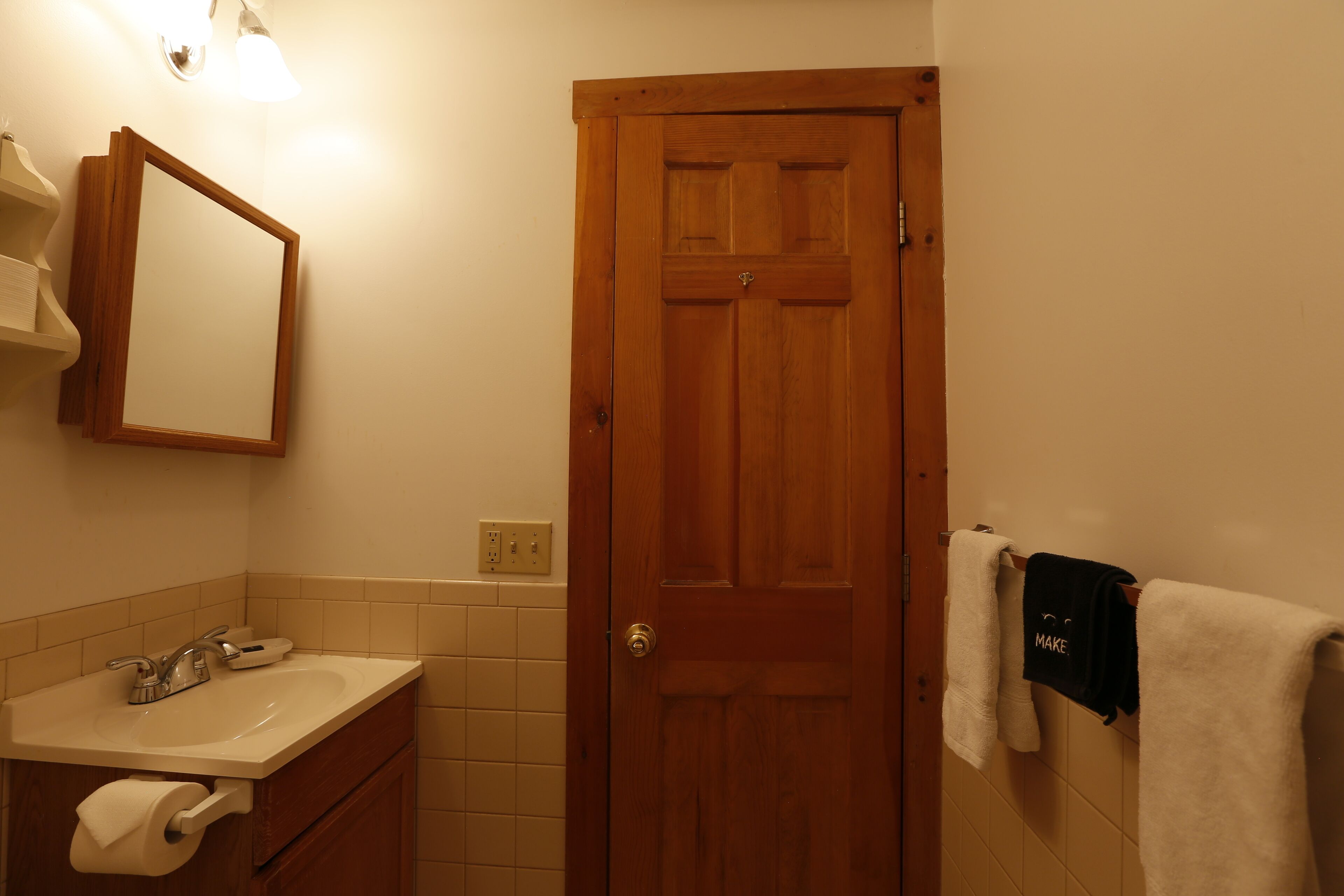 A bathroom with a wooden door, a sink with a mirror, and a towel rack with a towel.