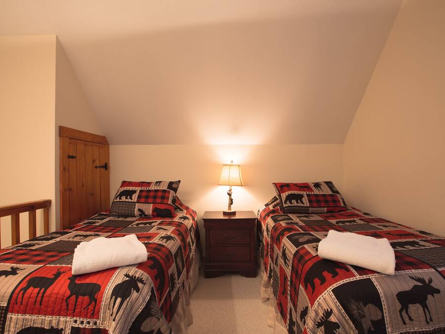 A bedroom with two beds, a nightstand, a lamp, and a wooden wardrobe.