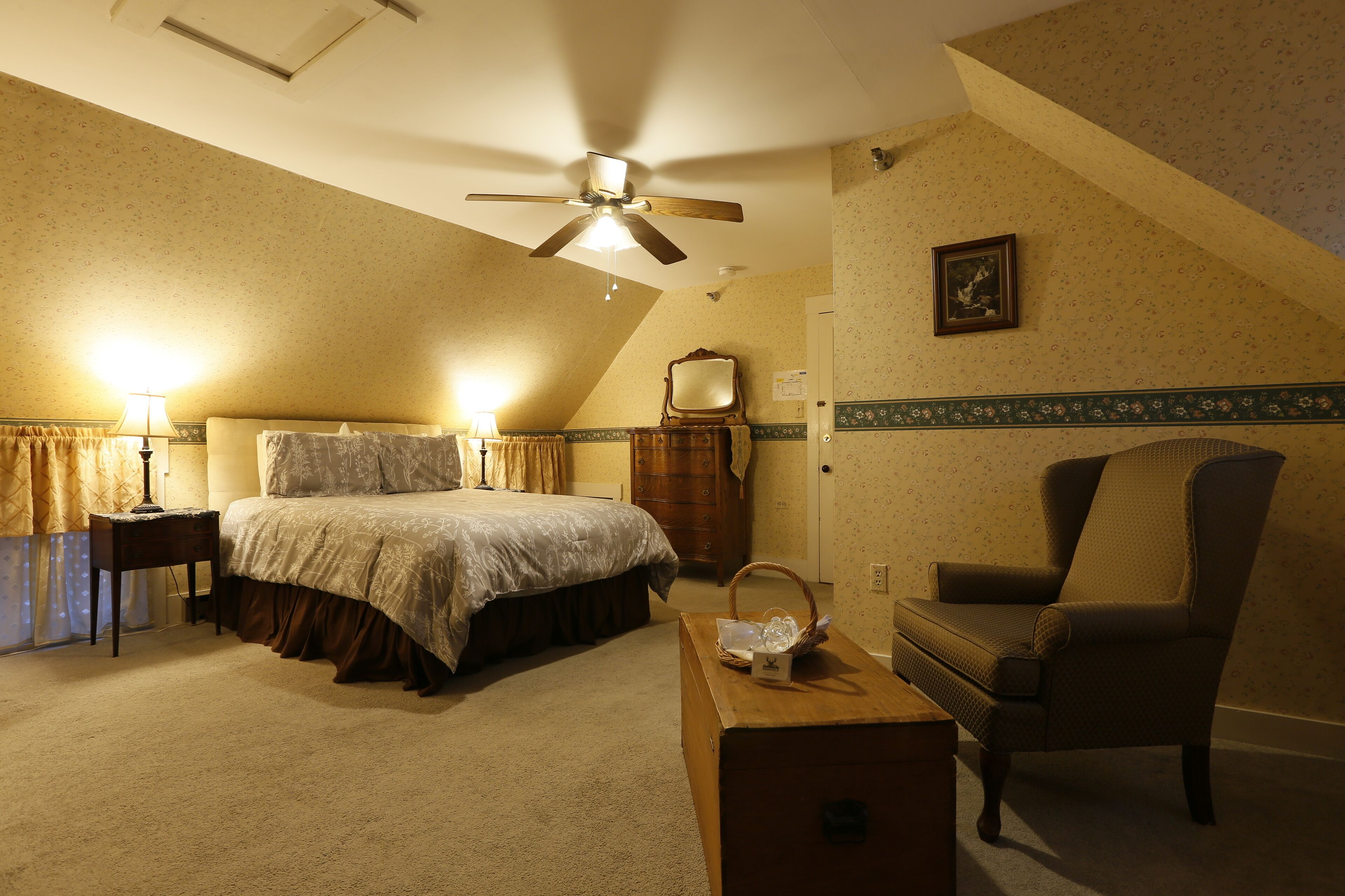 A bedroom with a bed, a chair, a nightstand, a dresser, a ceiling fan, and a picture on the wall.