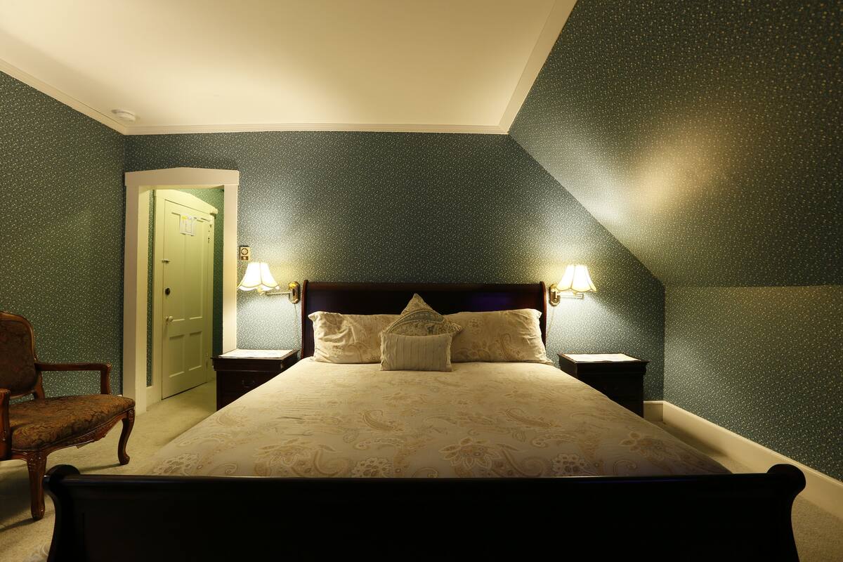 A bedroom with a bed, two nightstands, a chair, and a door.